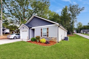 A single-story house with a garage, a front yard with a landscaped garden, and a clear sky.
