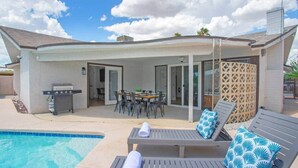 En overdækket terrasse med pool, liggestole, grill og spisebord.