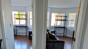 Uma sala de estar espaçosa com piso de madeira, um sofá cinza e uma mesa de escritório de metal preto.