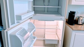 Uma geladeira aberta com várias prateleiras e gavetas, uma torradeira e uma cafeteira sobre a bancada.