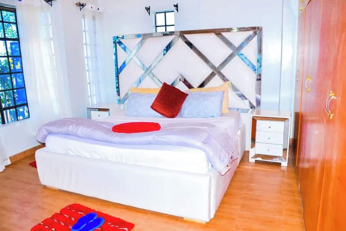 Ein modernes Schlafzimmer mit einem großen Bett, einem Holzkopfteil, einem Nachttisch, einem Kleiderschrank und einem Fenster mit Aussicht.