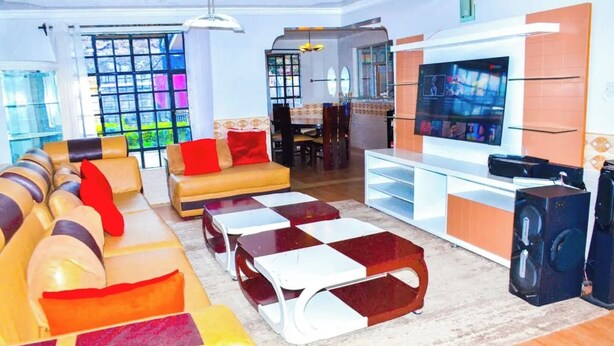 A modern living room with a sofa, coffee table, TV, and speakers. - Majestic Airport Villa (Syokimau)