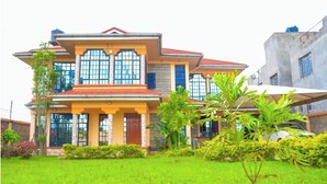 A two-story house with a large front porch, multiple windows, and a well-maintained lawn. - Majestic Airport Villa (Syokimau)