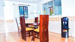 A dining area with a wooden table and chairs, a water dispenser, and a window with a view of the outside. - Majestic Airport Villa (Syokimau)