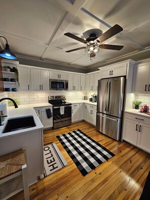 A modern kitchen with white cabinets, stainless steel appliances, a black and white checkered rug, and a ceiling fan. - 4-bedroom House with attached In-Law suite (Au Sable Forks)