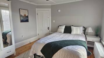 A bedroom with a bed, a ceiling fan, a nightstand, a mirror, and a door.