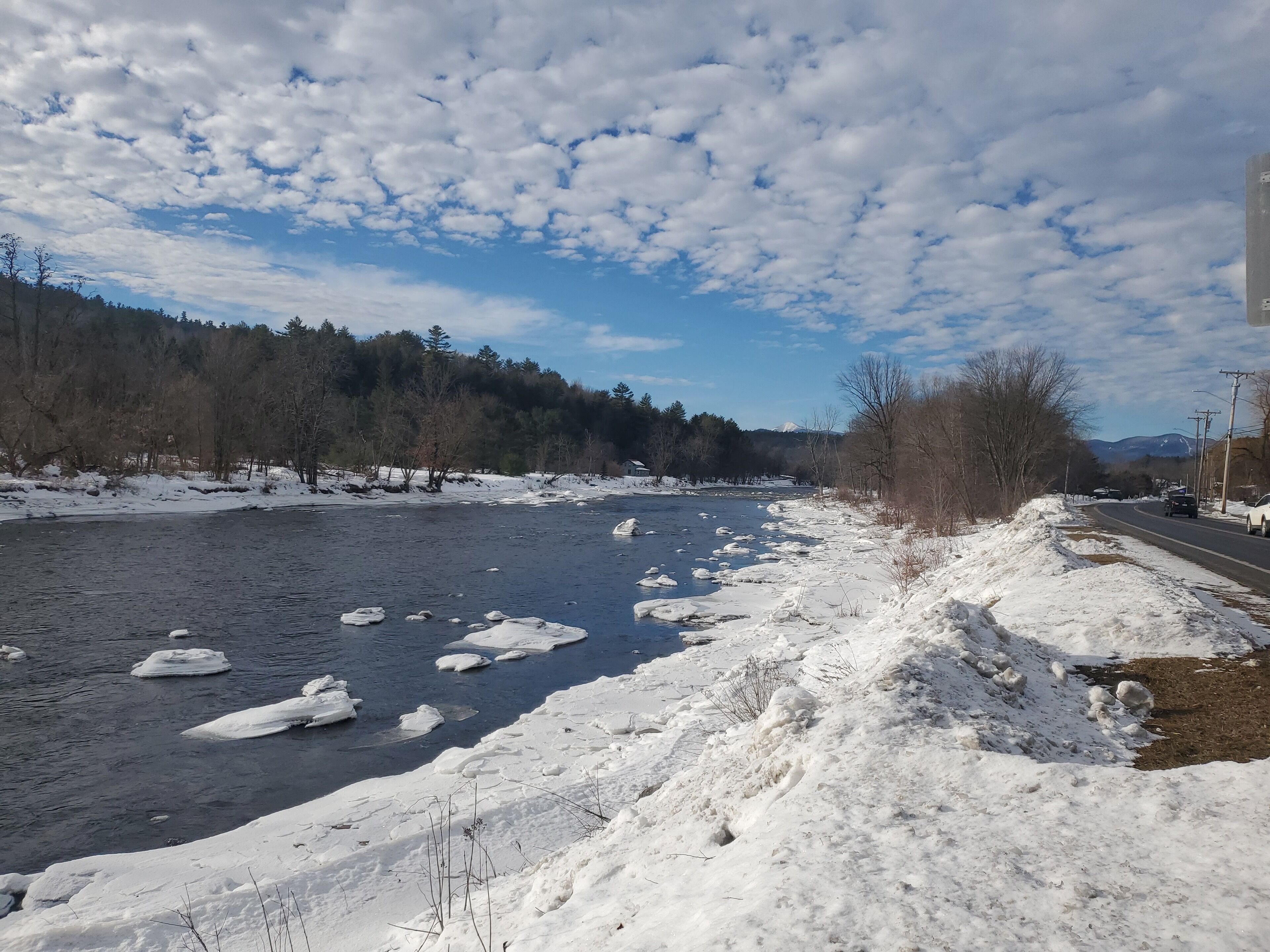 Ein Fluss mit Eisbergen, ein verschneiter Uferstreifen und eine Straße mit Fahrzeugen.