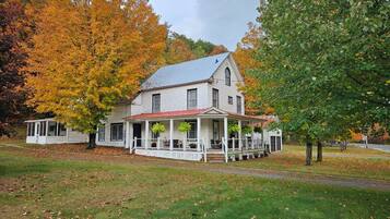 A two-story house with a porch, surrounded by trees with autumn foliage.