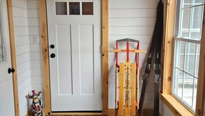 Een kamer met een witte deur, stenen vloer, houten balken en een raam met luiken.