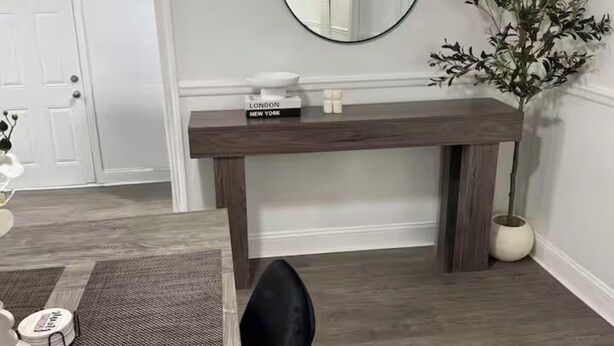 Een eetgedeelte met een houten tafel, zwarte stoelen, een ronde spiegel en een kamerplant.