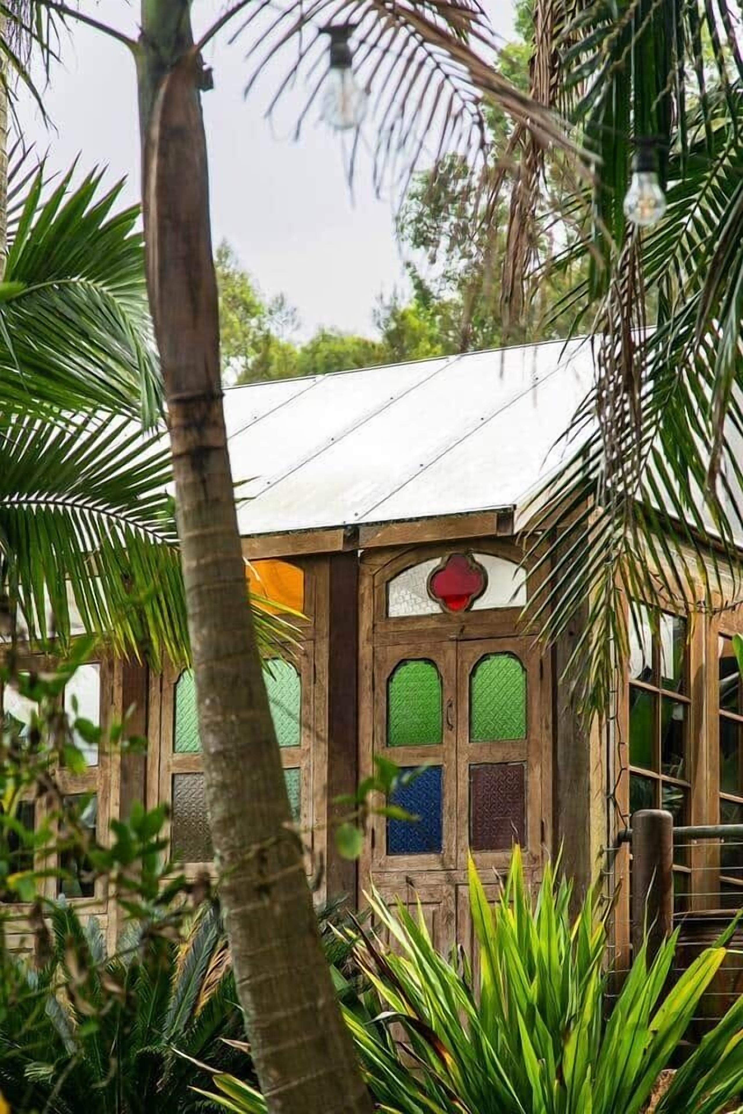 Un edificio rústico de madera con techo de paja, rodeado de vegetación exuberante y palmeras.