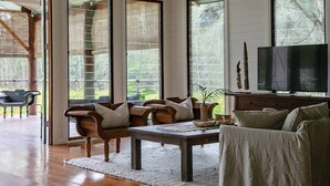 Un salon spacieux doté d’un plancher en bois, de grandes fenêtres, d’un téléviseur et d’un coin repas avec une table et des chaises.