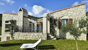 Un bâtiment en pierre avec un toit en tuiles, un balcon et une pelouse agrémentée d’une chaise longue.