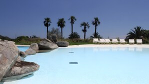 Une piscine d’eau cristalline, avec des rochers et des palmiers en arrière-plan.