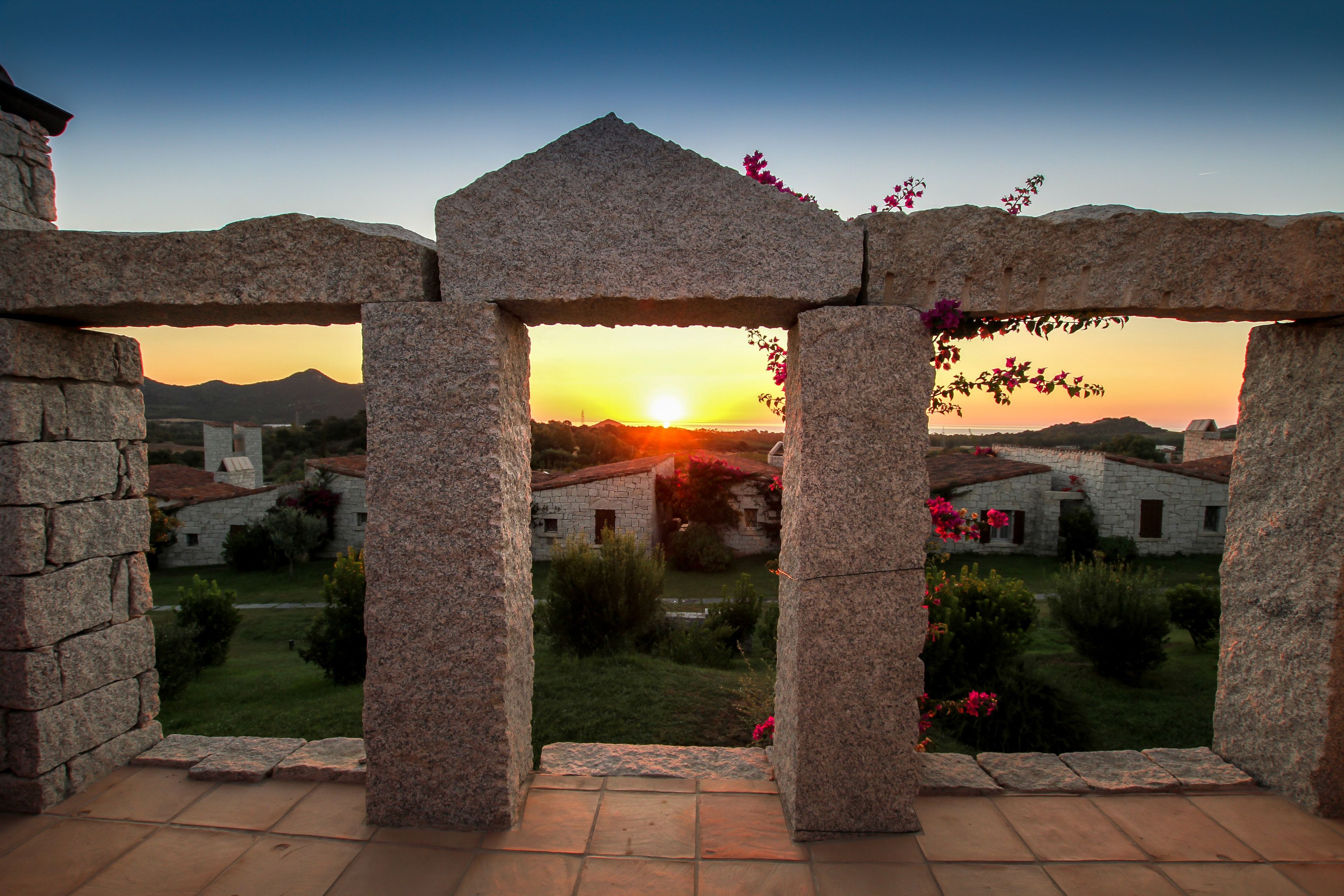 A stone archway framing a sunset view over a village with traditional buildings.