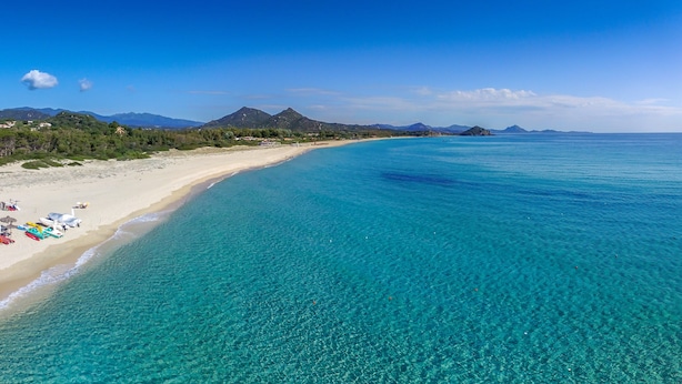 Una platja amb aigua turquesa cristal·lina, una riba sorrenca i muntanyes al fons.