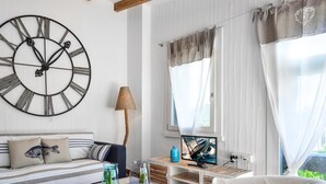 Habitació amb un rellotge de paret gran, un sofà, una taula amb objectes decoratius, una làmpada i una finestra amb cortines.