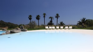 Una piscina de blau clar amb gandules blanques i palmeres al fons.