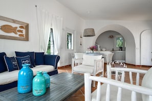 Una habitación con un sofá blanco, una mesa de comedor y una zona de cocina visible a través de un arco.