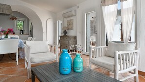 A room with white furniture, a table with two vases, and a window with curtains. - Li Conchi 35 – Spacious Holiday Home for 7 in a Modern Resort (Castiadas)