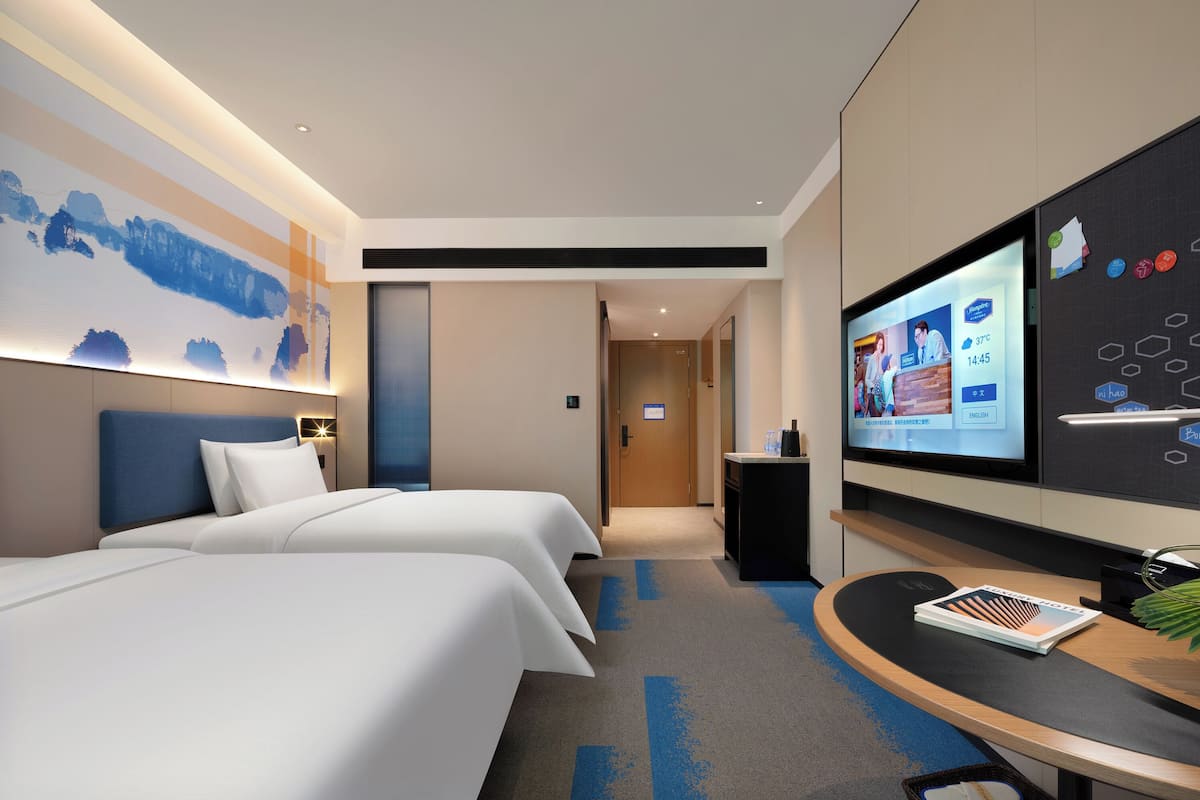 Ein Hotelzimmer mit zwei Betten, einem Schreibtisch und einem Flachbildfernseher, sowie einem großen Wandbild.
