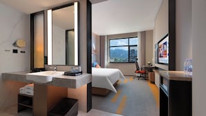 A hotel room with a large mirror, a bed, a desk, a chair, a TV, and a view of mountains. - Hampton by Hilton Zhangjiajie National Forest Park (Zhangjiajie)