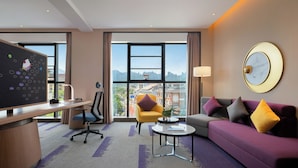 A modern hotel room with a large desk, a comfortable sofa, a small coffee table, and a view of the cityscape through large windows. - Hampton by Hilton Zhangjiajie National Forest Park (Zhangjiajie)