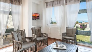 Una habitación con sillas de mimbre, una mesa con bandeja y un televisor en la pared.