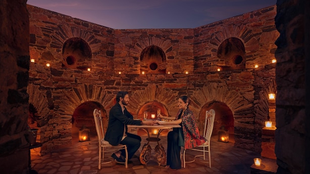 Un comedor de paredes de piedra con una mesa y sillas, iluminado por velas.