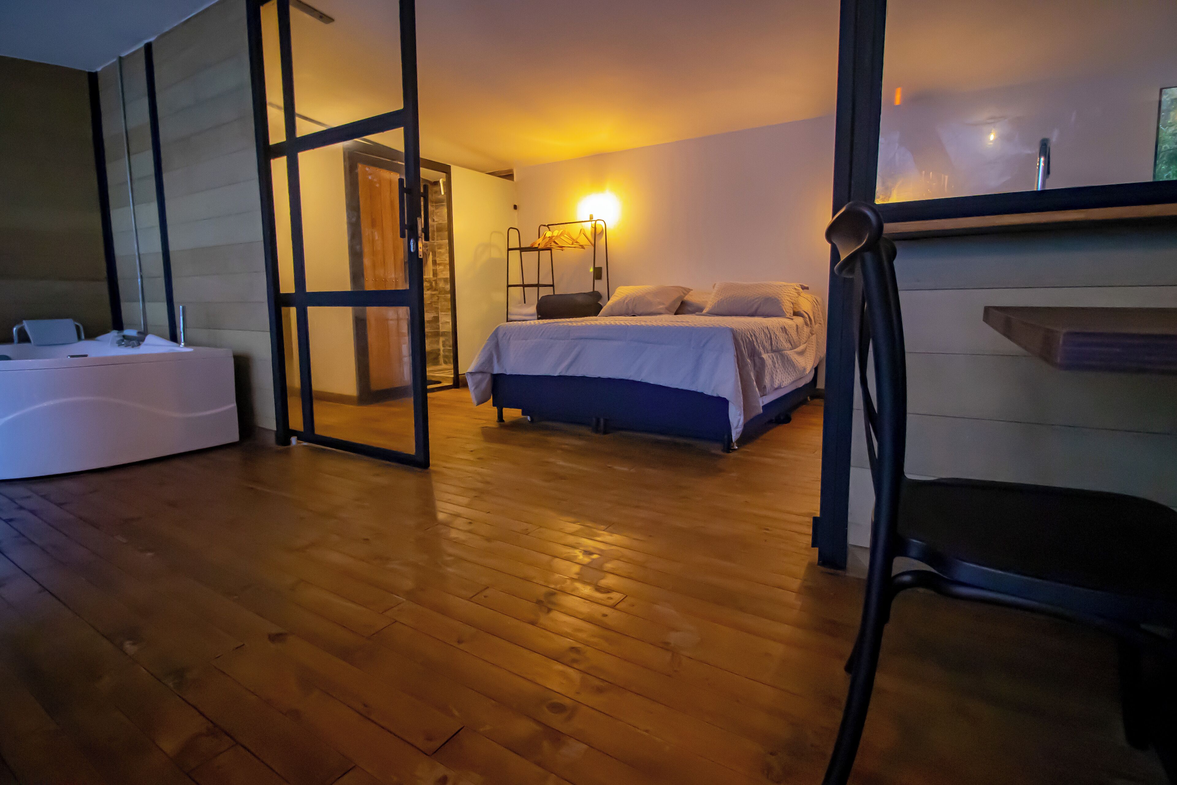 Un dormitorio con suelo de madera, una cama, una mesita de noche y una lámpara fijada a la pared.