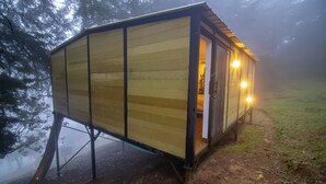 A wooden cabin with a single door and two windows, elevated on stilts near a body of water. - Forest cabin located in the mountain with Jacuzzi (Versalles)