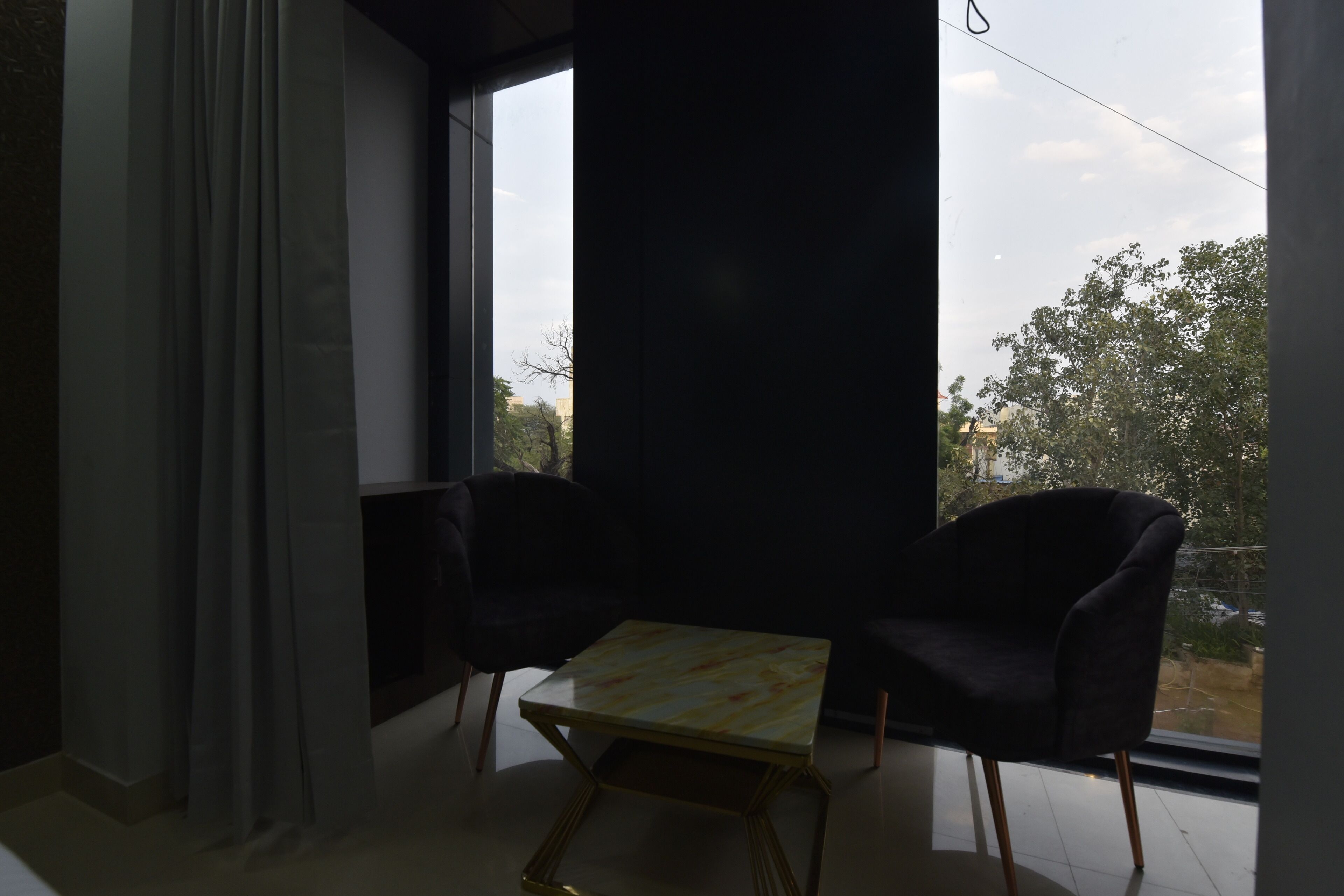 A room with two black chairs, a small table, and a large window offering a view of trees and buildings.