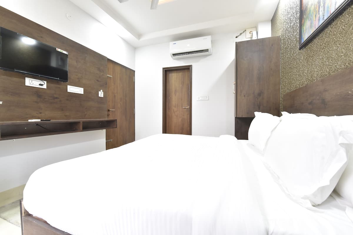 A bedroom with a large bed, wooden wardrobe, and a mounted TV.