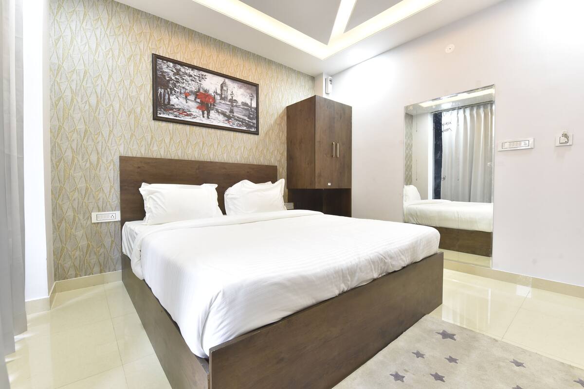 A bedroom with a large bed, a wardrobe, a window with curtains, and a wall-mounted picture.