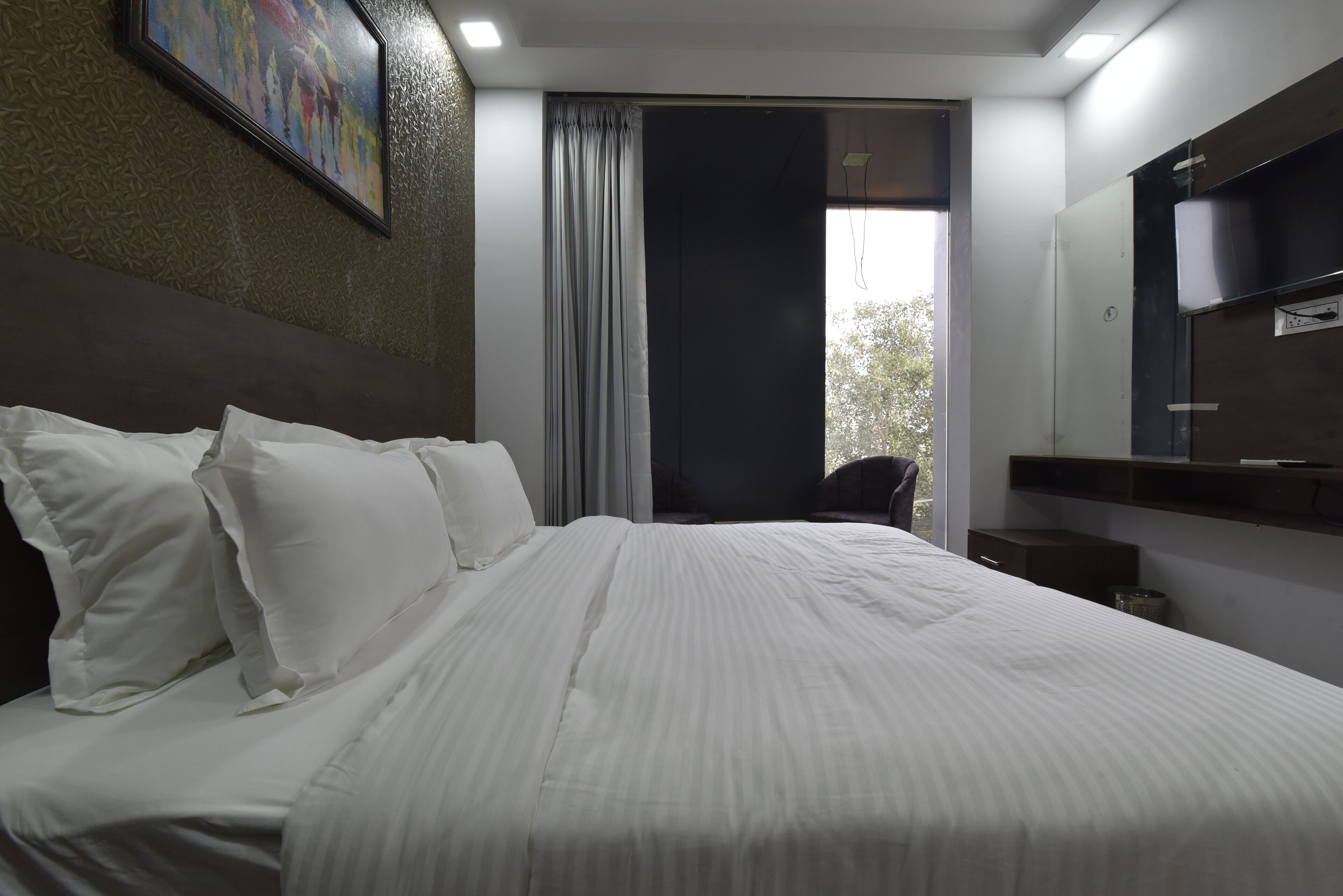 Quarto de hotel com uma cama grande, cortina escura, janela e televisão presa à parede.