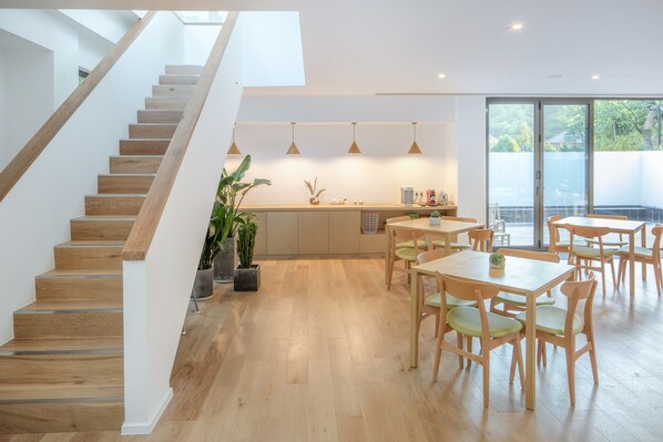 Una cocina moderna con suelo de madera, una escalera y un comedor con mesas y sillas de madera.
