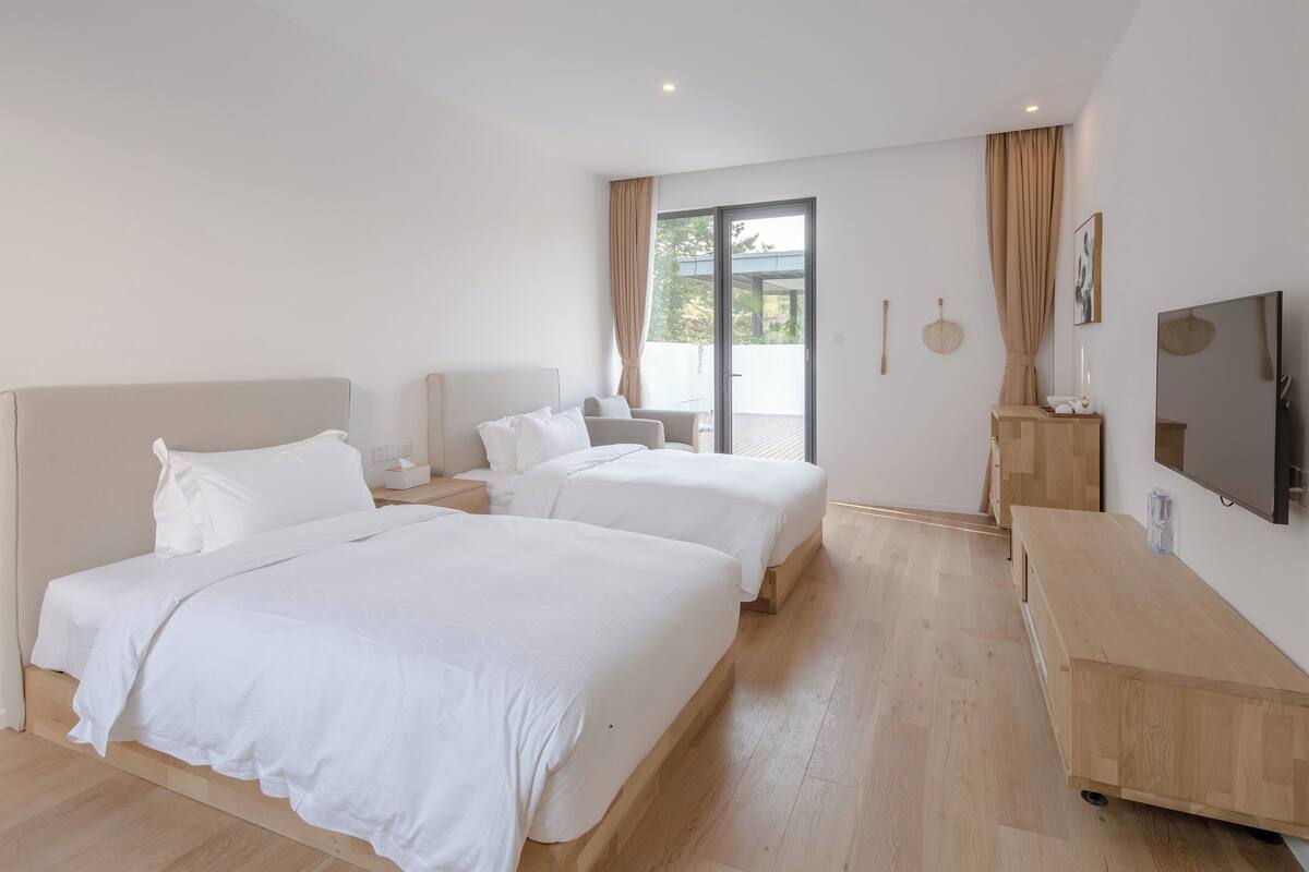 Una habitación de hotel moderna con dos camas, un aparador de madera, un televisor de pantalla plana y una puerta corrediza de vidrio al exterior.