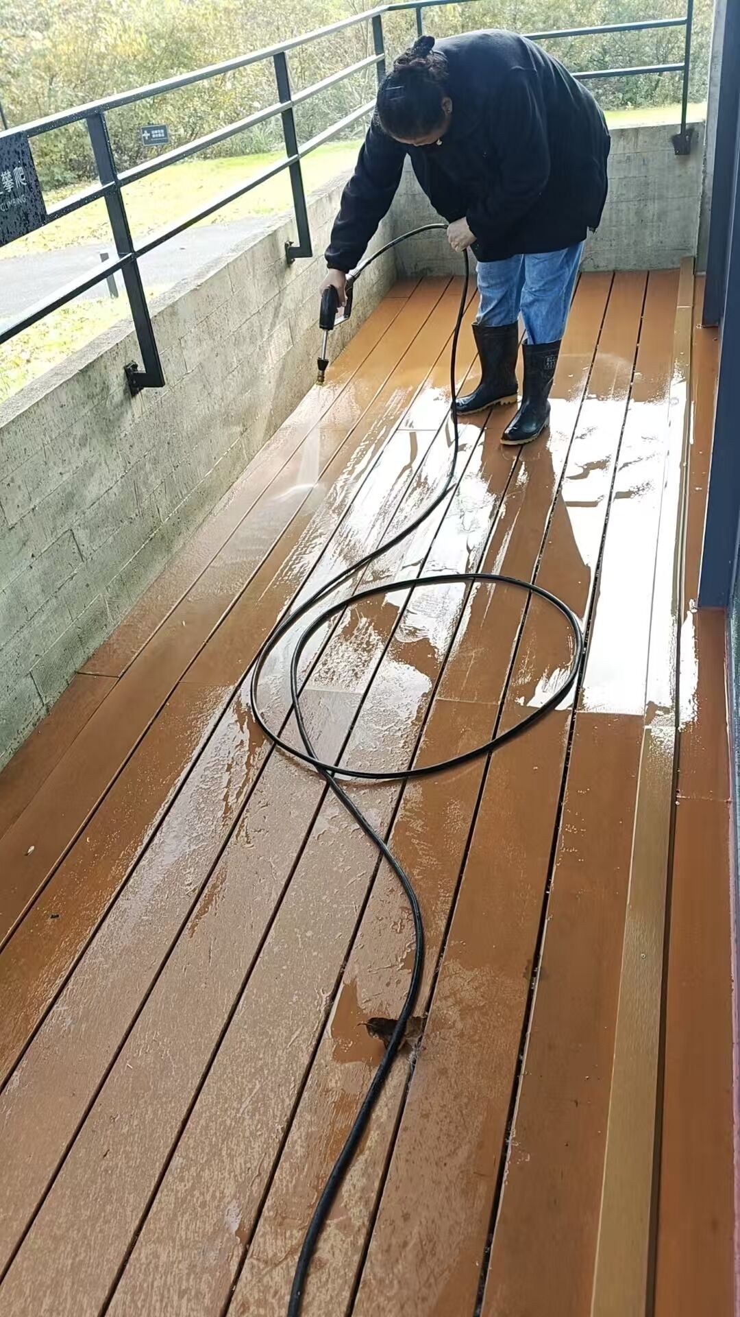A person cleaning a wooden deck with a hose.