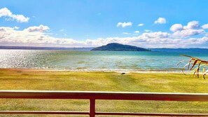 Une vue d’un lac avec une île au loin, une zone herbeuse et une clôture en bois au premier plan.