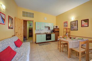 Un espacio habitable compacto con kitchenette, comedor y sofá con cojines rojos.
