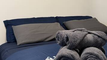 Una cama con cubrecama azul, almohadas grises y una pila de toallas grises. Tres obras enmarcadas de Henri Matisse están exhibidas en la pared sobre la cama.