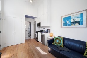 Ein modernes Wohnzimmer mit einer schwarzen Ledersofa, einem kleinen weißen Schreibtisch und einer Küchenzeile im Hintergrund.