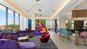 Un hall d’hôtel moderne doté d’un grand espace salon, d’un bar et d’une fresque murale aux couleurs vives.