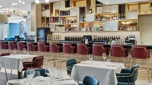Un restaurant doté de nombreuses tables et chaises, d’un bar avec des étagères remplies de bouteilles et d’un luminaire décoratif au plafond.