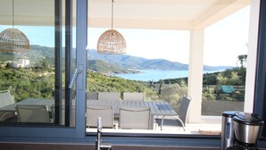 Eine moderne Küche mit Blick auf eine Küstenlandschaft, ein Essbereich mit Außenbestuhlung und einer Pendelleuchte.