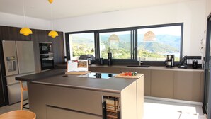 A modern kitchen with a large island, built-in appliances, and a view of a mountainous landscape. - Villa d'exception piscine privée 🏝️ 300m² - 16 pers Promo en cours (Pietrosella)