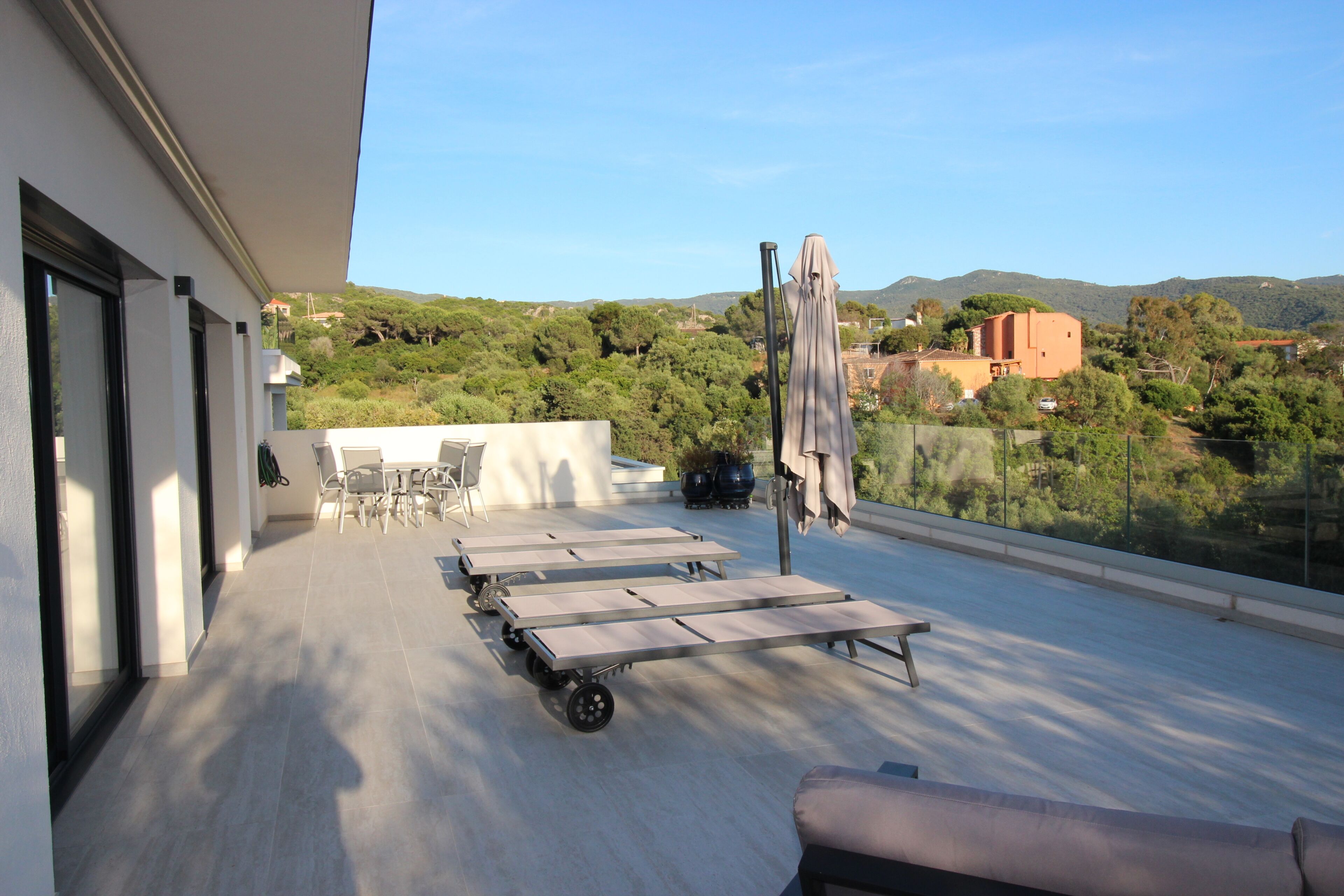 A rooftop terrace with a dining area, lounge chairs, and a view of the surrounding landscape.