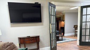 A living room with a brown leather sofa, a wooden coffee table, and a flat-screen TV mounted on the wall. - The Cardinal House 1B in charming Savannah (Savannah)