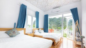 A hotel room with two beds, a wooden headboard, a nightstand, a fan, and a view of greenery through large windows. - Cat Ba Countryside Homestay (Hai Phong)