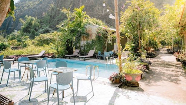 A poolside area with lounge chairs and tables, surrounded by lush greenery and a mountain backdrop. - Cat Ba Countryside Homestay (Hai Phong)